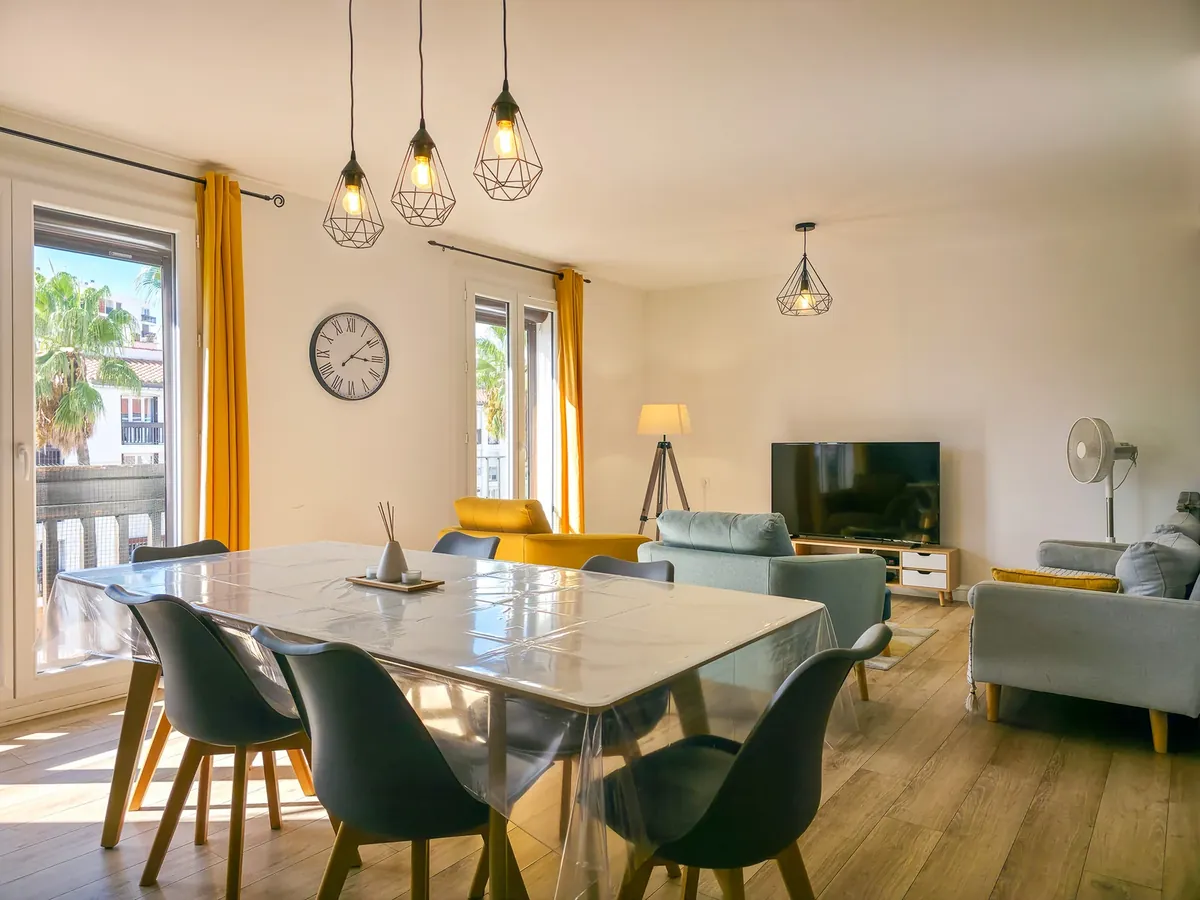 Séjour lumineux avec table dressée, chaises vertes et rideaux jaunes