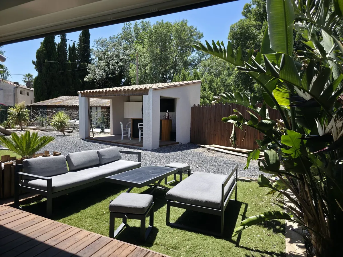 Terrasse avec salon de jardin gris et végétation autour du bassin